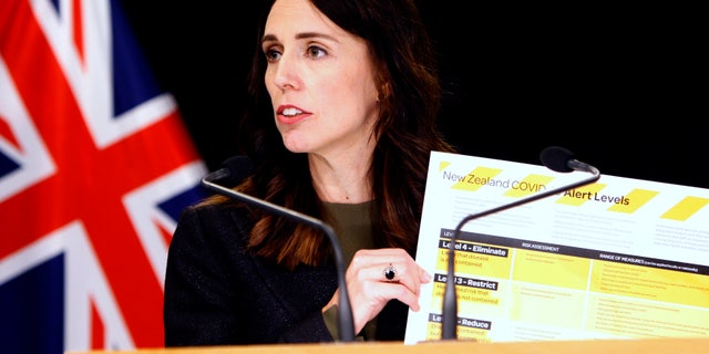 New Zealand Prime Minister Jacinda Ardern holds up a card showing a new alert system for COVID-19. (AP)