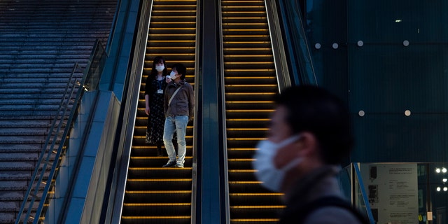 Wearing protective masks to help reduce the spread of the coronavirus, commuters ride an escalator Monday, April 6, 2020, in Tokyo.