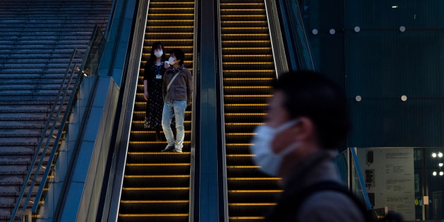 Wearing protective masks to help reduce the spread of the coronavirus, commuters ride an escalator Monday, April 6, 2020, in Tokyo.