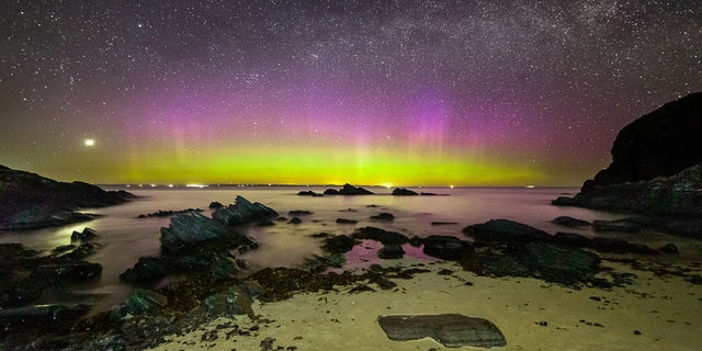 Bright purple and green aurora shine under the Milky Way at Noss Head near Wick in Scotland.