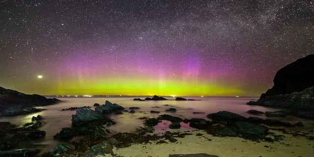 Bright purple and green aurora shine under the Milky Way at Noss Head near Wick in Scotland.