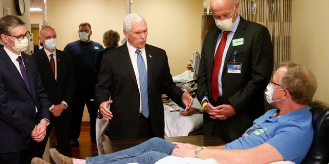 Vice President Mike Pence, who chose not to wear a face mask while touring the Mayo Clinic in Minnesota on Tuesday, visits Dennis Nelson, a patient who survived the coronavirus and was going to give blood.