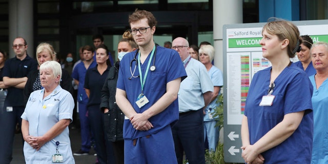 Staff stand outside Salford Royal Hospital in Manchester, England, Tuesday April 28, 2020, during a minute's silence to pay tribute to the NHS staff and key workers who have died during the coronavirus outbreak. (Peter Byrne/PA via AP)