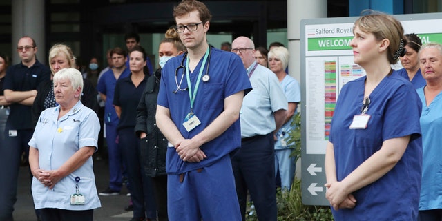 Staff stand outside Salford Royal Hospital in Manchester, England, Tuesday April 28, 2020, during a minute's silence to pay tribute to the NHS staff and key workers who have died during the coronavirus outbreak. (Peter Byrne/PA via AP)