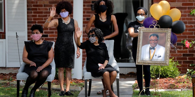 The family of Larry Hammond wave as a line of cars with friends and family, who could not attend his funeral because of limits of gatherings of more than 10 people, due to the coronavirus pandemic, pass by their home, in New Orleans, April 22. (AP Photo/Gerald Herbert)