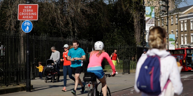 People observe social distancing as they pass by the locked gates to Brockwell Park in London after it was closed overnight to help stop the spread of coronavirus.