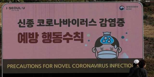 People wearing face masks pass by an electric screen about precautions against the COVID-19 illness at the Dongdaemun Design Plaza in Seoul, South Korea, Tuesday.