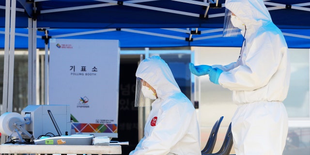 Election officials wearing protective gears, wait for voters during an early voting for the April 15 general elections at a special polling station set up for coronavirus patients and medical members at a treatment center in Yongin, South Korea.