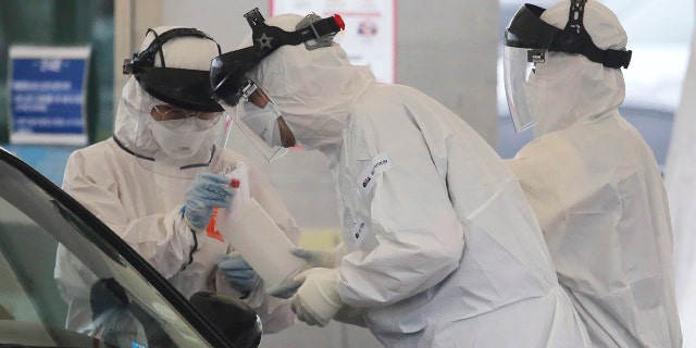 In this March 1, 2020 file photo, medical staff wearing protective suits take samples from a person with suspected symptoms of the new coronavirus at a drive-thru virus test facility in Goyang, South Korea.