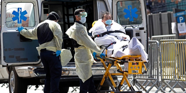 'Terrified' doctors risking their health fighting coronavirus dealt another blow -- pay cuts 2 A patient is wheeled out of Elmhurst Hospital Center to a waiting ambulance, Tuesday, April 7, 2020, in the Queens borough of New York, during the current coronavirus outbreak. New York Gov. Andrew Cuomo said last week that as city hospitals fill up, some patients could be moved to other facilities in the state to ease the crunch on local medical centers. (AP Photo/Kathy Willens)