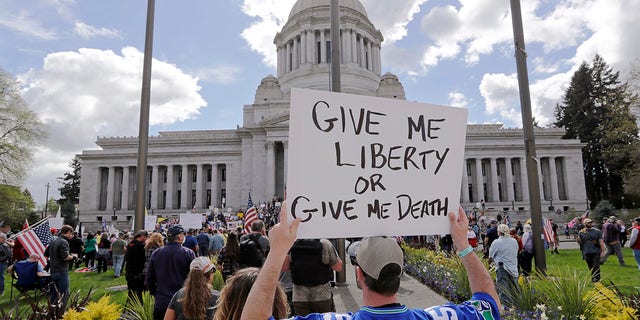 A man holds a sign in view of the Capitol building at a protest opposing Washington state's stay-home order to slow the coronavirus outbreak Sunday, April 19, 2020, in Olympia, Wash. (AP Photo/Elaine Thompson)