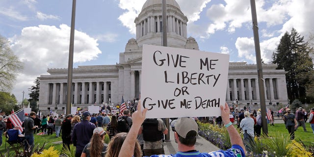 A man holds a sign in view of the Capitol building at a protest opposing Washington state's stay-home order to slow the coronavirus outbreak Sunday, April 19, 2020, in Olympia, Wash. Washington Gov. Jay Inslee has blasted President Donald Trump's calls to 