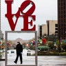 A person wearing a protective face mask and gloves as a precaution against the coronavirus walks by the Robert Indiana sculpture "LOVE" at John F. Kennedy Plaza in Philadelphia, April 13, 2020.