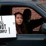 A passenger in a vehicle holds a sign during the protest at the State Capitol in Lansing, Michigan.