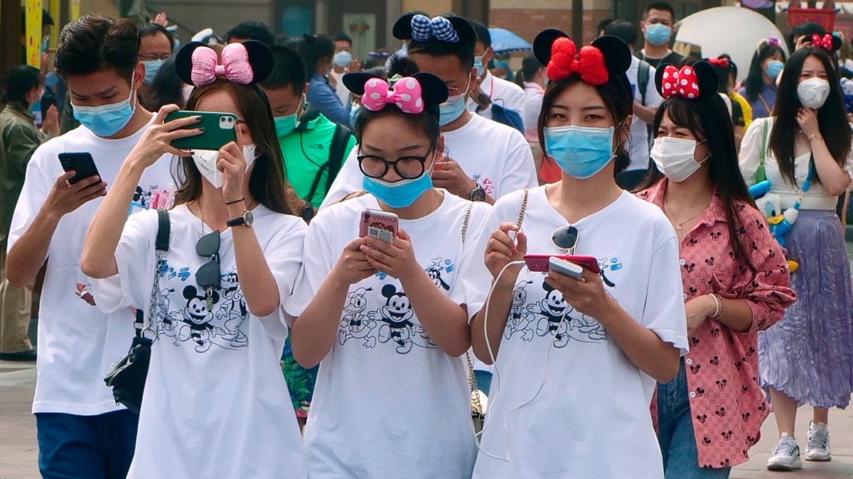 Visitors, wearing face masks, enter the Disneyland theme park in Shanghai as it reopened, Monday, May 11, 2020. Visits will be limited initially and must be booked in advance, and the company said it will increase cleaning and require social distancing in lines for the various attractions.(AP Photo/Sam McNeil)