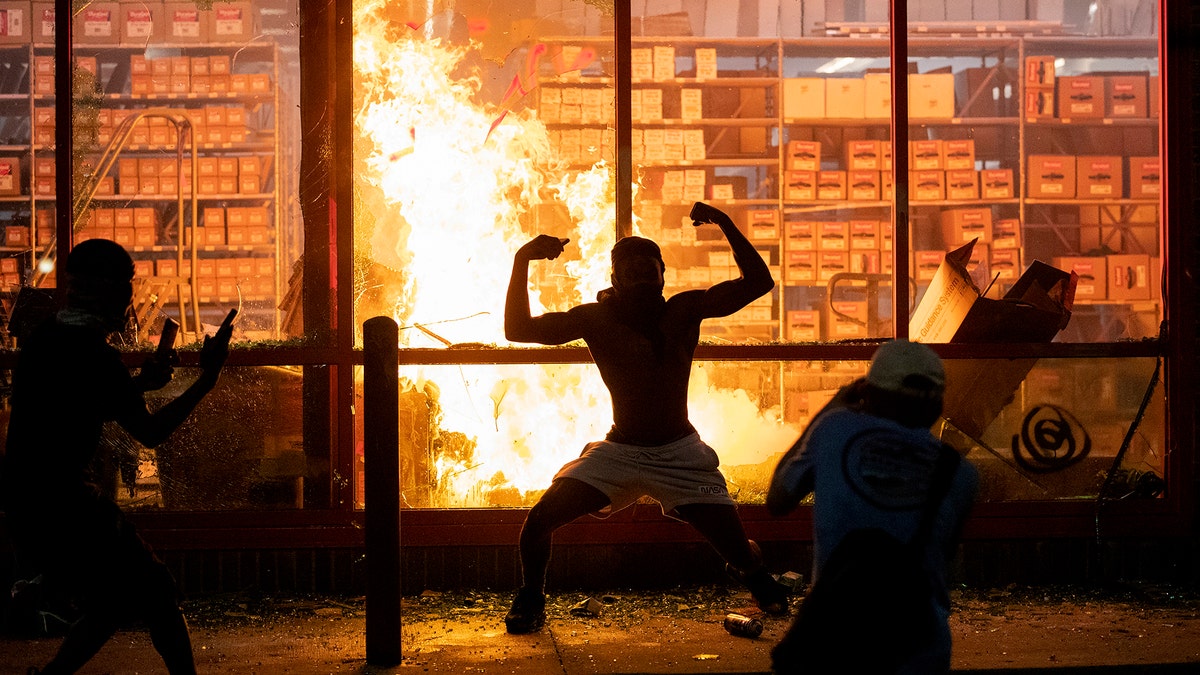 A man poses for photos in front of a fire at an AutoZone store, while protesters hold a rally for George Floyd in Minneapolis on Wednesday, May 27, 2020. Violent protests over the death of the black man in police custody broke out in Minneapolis for a second straight night Wednesday, with protesters in a standoff with officers outside a police precinct and looting of nearby stores. (Carlos Gonzalez/Star Tribune via AP)