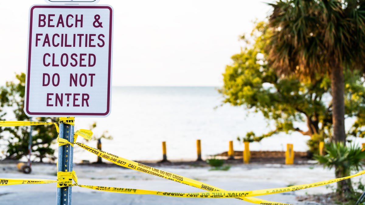 Beach, facilities closed, do not enter sign post by coast, shore after destruction of hurricane Irma with nobody, yellow tape, road in key island, Florida, palm trees