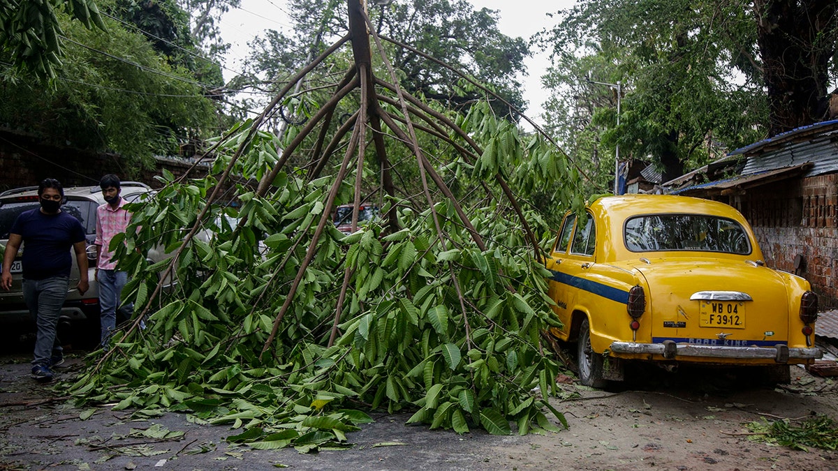 People walk past a tree branch fallen in the middle of a road after Cyclone Amphan hit the region in Kolkata, India, Thursday, May 21, 2020.