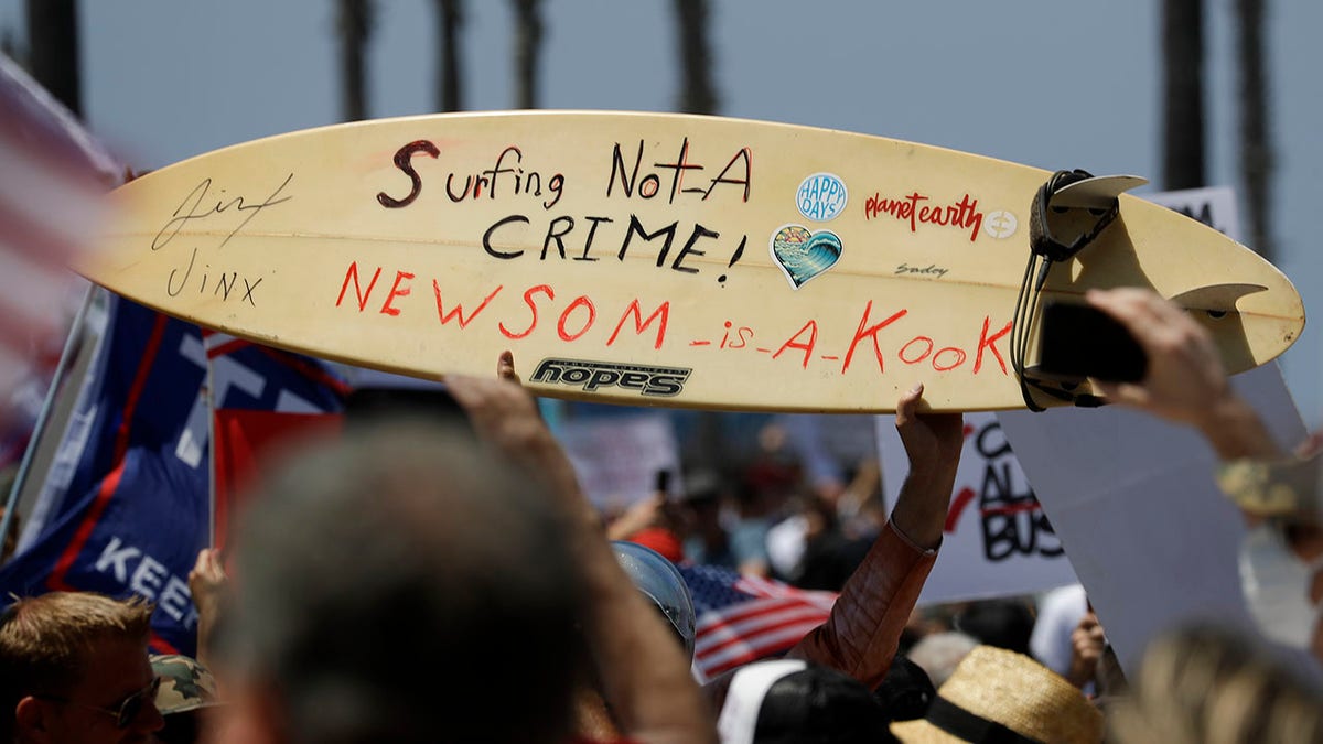 A protestor holds a hand painted sign on a surfboard during a demonstration at the pier, Friday, May 1, 2020, in Huntington Beach, Calif. (Associated Press)