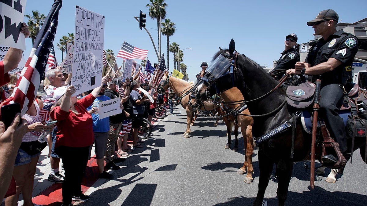 Law-enforcement personnel on horseback keep protesters on the sidewalk during a demonstration on May Day at the pier during the coronavirus pandemic Friday, May 1, 2020, in Huntington Beach, Calif.