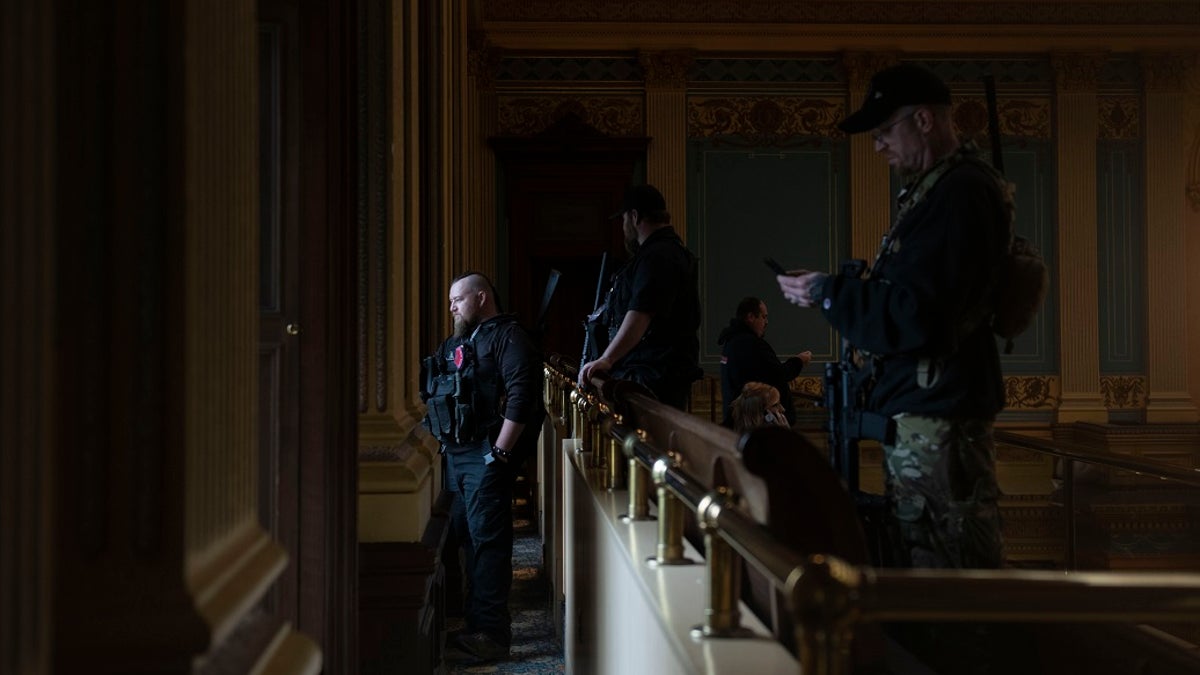 Members of a militia group watch the protest outside while waiting for the Michigan Senate to vote at the Capitol in Lansing, Mich. Gun-carrying protesters have been a common sight at some demonstrations calling for coronavirus-related restrictions to be lifted. But an armed militia’s involvement in an angry protest in the Michigan statehouse Thursday marked an escalation that drew condemnation and shone a spotlight on the practice of bringing weapons to protest. (Nicole Hester/MLive.com/Ann Arbor News via AP)