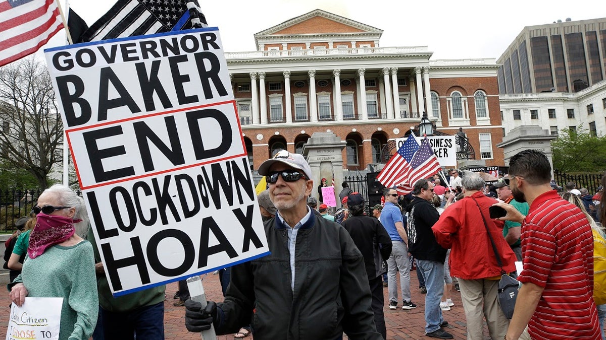 Demonstrators display flags and placards during a protest Monday in front of the Statehouse, in Boston. Protesters gathered in front of the Statehouse Monday to protest restrictions on movement and businesses prompted by the COVID-19 outbreak. (AP Photo/Steven Senne)