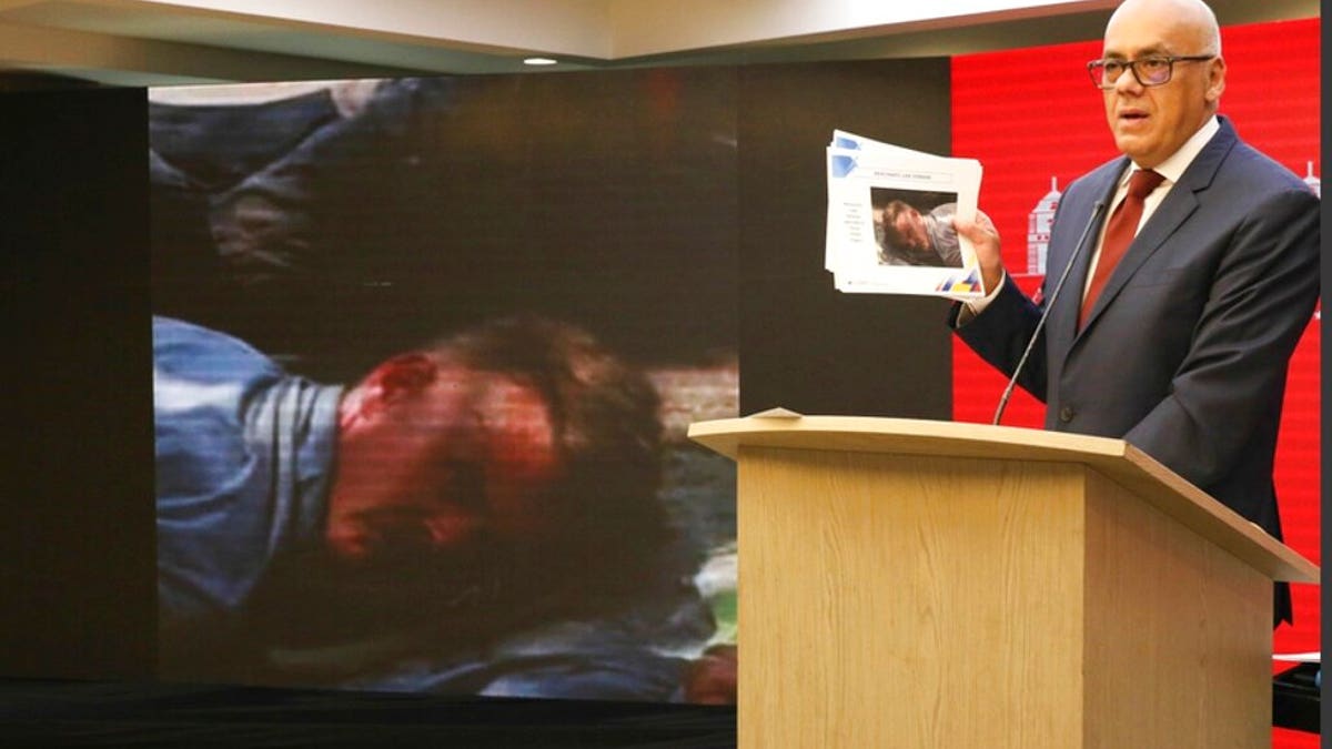 In this photo released by the Venezuelan Communications Ministry press office, Communications Minister Jorge Rodriguez shows a photograph of a man he identifies as former U.S. special forces soldier Luke Denman and taken in Venezuela during his arrest, in Caracas, Venezuela, Tuesday, May 5, 2020. Venezuelan authorities say they arrested Denman and one other U.S. citizen among a group of “mercenaries” on Monday, a day after a beach raid purportedly aimed at capturing the leader that Venezuelan authorities say they foiled.