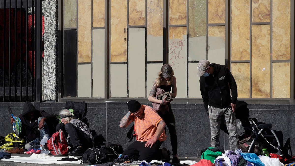 People sit and gather with belongings on a sidewalk in San Francisco on April 21, 2020. The city's homeless continue to sleep on the sidewalks and flap-to-flap in tents cluttered downtown and in other popular neighborhoods. (AP Photo/Jeff Chiu)