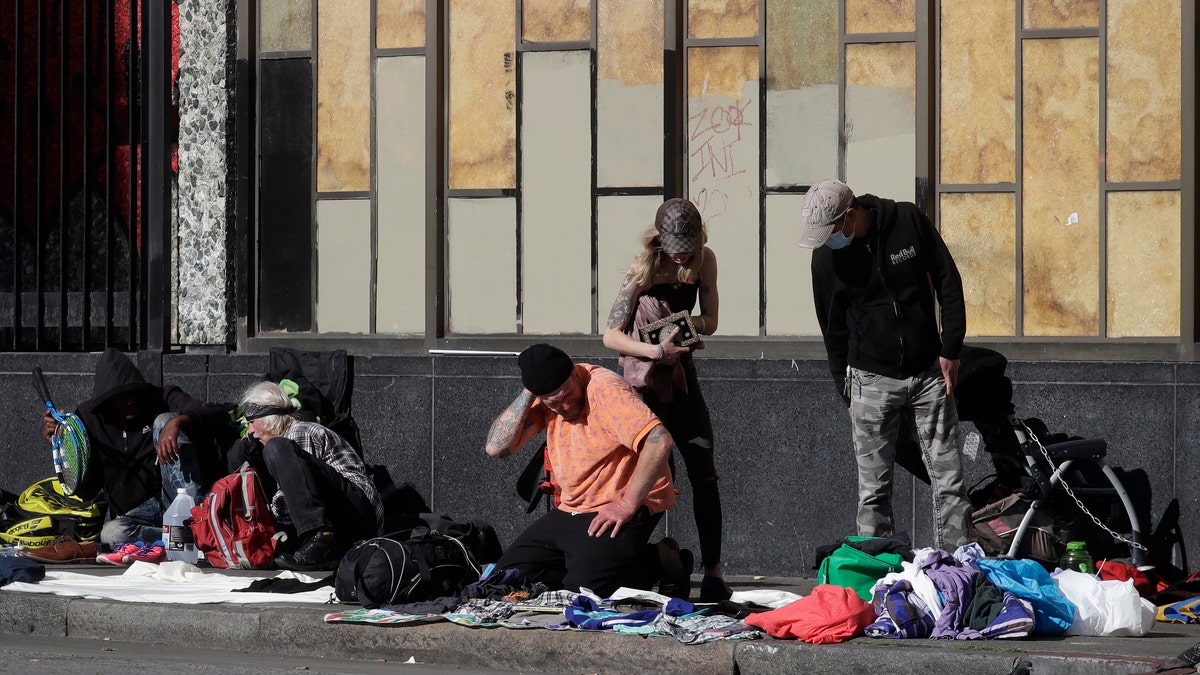 People sit and gather with belongings on a sidewalk in San Francisco on April 21, 2020. The city's homeless continue to sleep on the sidewalks and flap-to-flap in tents cluttered downtown and in other popular neighborhoods. (AP Photo/Jeff Chiu)