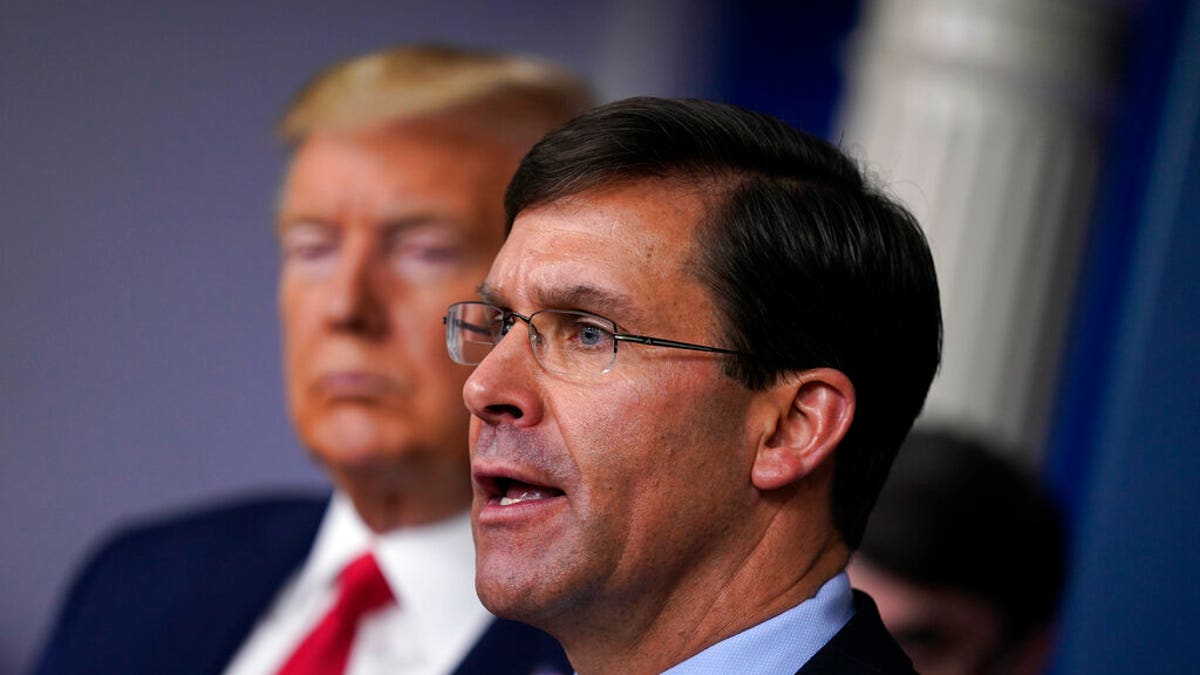 FILE - In this March 18, 2020, file photo, Defense Secretary Mark Esper speaks as President Donald Trump listens during press briefing with the coronavirus task force, at the White House in Washington. The government’s $3 trillion effort to rescue the economy from the coronavirus crisis is stirring worry at the Pentagon. Bulging federal deficits may force a reversal of years of big defense spending gains and threaten prized projects like the rebuilding of the nation’s arsenal of nuclear weapons. Esper says the sudden burst of emergency spending to prop up a stalled economy is bringing the Pentagon closer to a point where it will have to shed older weapons faster and tighten its belt. (AP Photo/Evan Vucci, File)