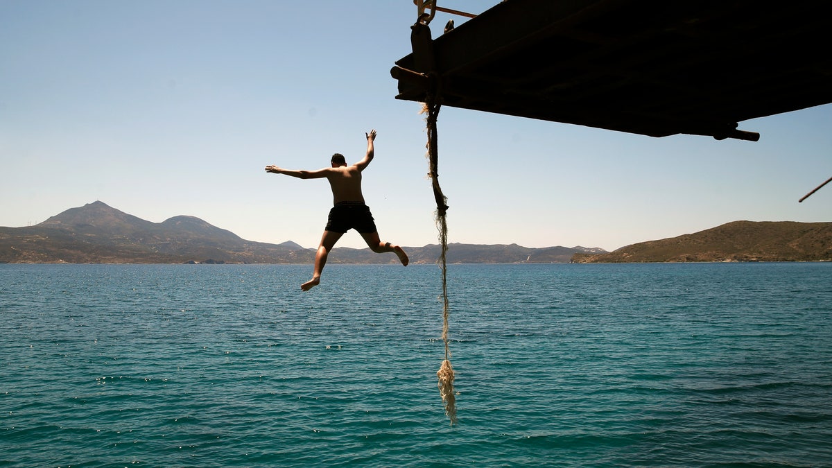 A boy dives into the sea from an old dock on the Aegean Sea island of Milos, Greece, Sunday, May 24, 2020. Greece's long-awaited tourist season will begin on June 15 with the opening of seasonal hotels and the arrival of the first foreign visitors, while international flights will begin heading directly for holiday destinations gradually as of July 1. (AP Photo/Thanassis Stavrakis)