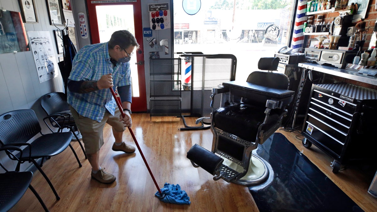 Mike Douglass, owner of the East J Barbershop, mops the floor of his shop on May 27 in Sacramento, Calif. Douglass said he will reopen in a few days so he has time to get his shop ready to adhere to the new guidelines that must be followed due to the coronavirus pandemic. (AP Photo/Rich Pedroncelli)