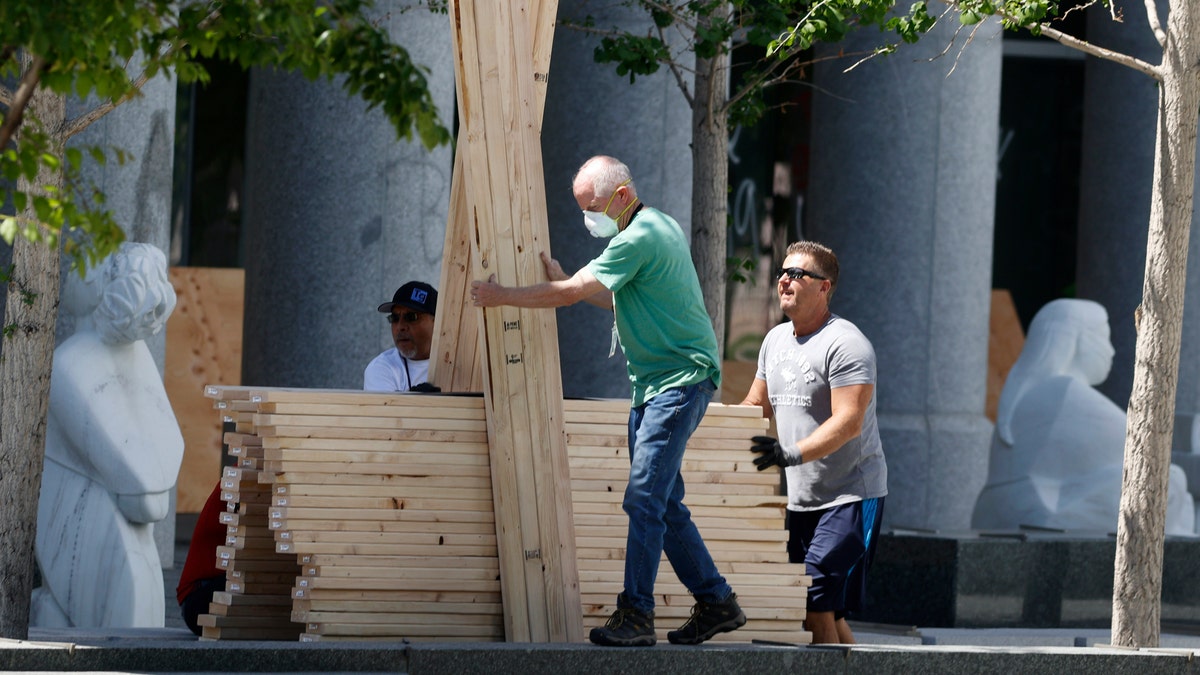 Workers move a cart of planks to use in the repair of windows destroyed after a protest outside the State Capitol over the death of George Floyd, a handcuffed black man in police custody in Minneapolis, turned into a melee between protesters and the police Saturday, May 30, 2020, in Denver. (AP Photo/David Zalubowski)