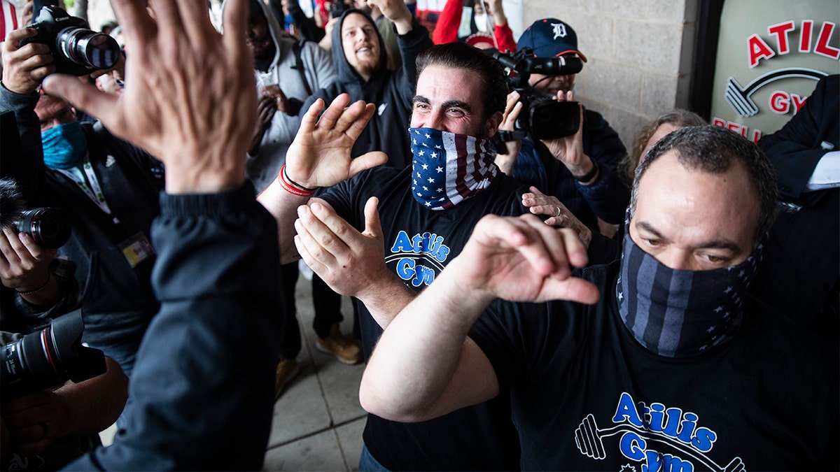 Atilis Gym co-owners Frank Trumbetti, center right, and Ian Smith, center, react after meeting with a police officer outside their gym in Bellmawr, N.J., Monday, May 18, 2020. The gym in New Jersey reopened for business early Monday, defying a state order that shut down nonessential businesses to help stem the spread of the coronavirus. (AP Photo/Matt Rourke)