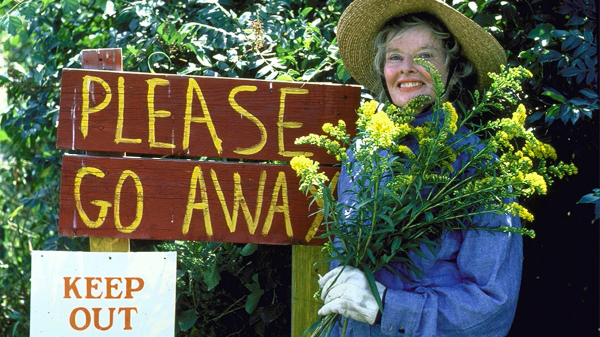 Actress Katharine Hepburn next to a homemade sign saying Go Away in her driveway. 