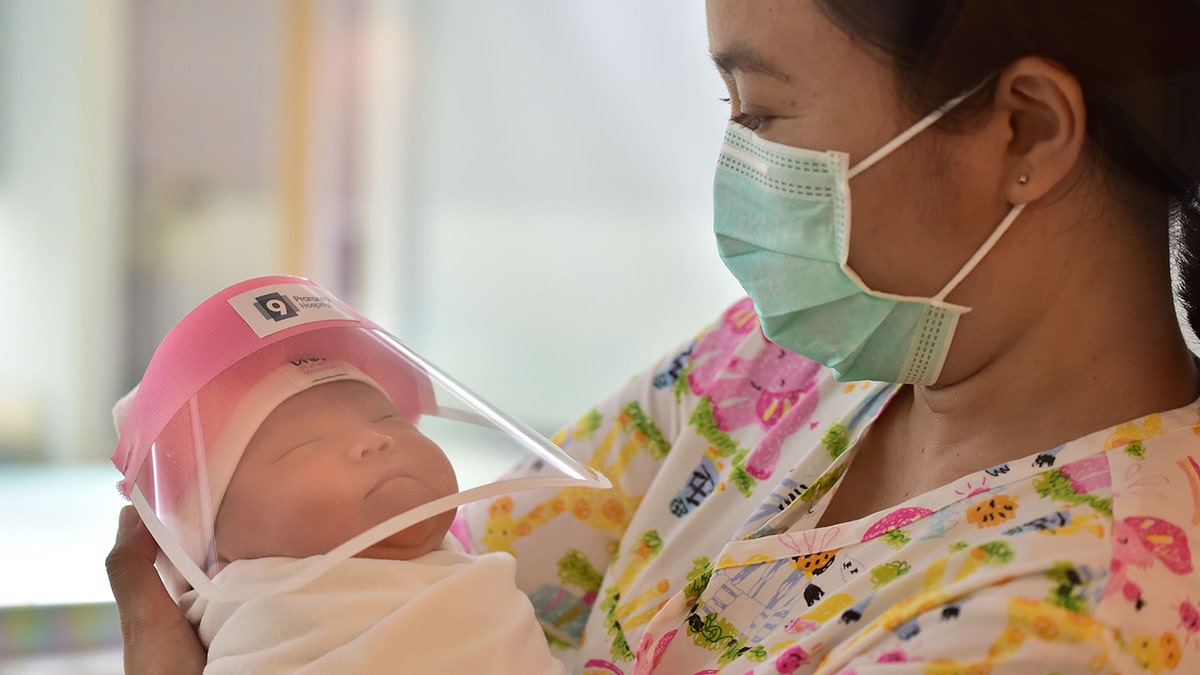 This photo taken through a glass window at a maternity ward shows a nurse holding a newborn baby wearing a face shield, in an effort to halt the spread of the COVID-19 coronavirus, at Praram 9 Hospital in Bangkok on April 9, 2020. (Photo by Lillian SUWANRUMPHA / AFP) (Photo by LILLIAN SUWANRUMPHA/AFP via Getty Images)