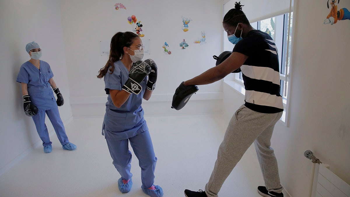 In this Wednesday, May 27, 2020 photo, medical worker Kenza, center and Nassima, left, attend a training with French boxer Hassan N’Dam at the Villeneuve-Saint-Georges hospital, outside Paris. A world champion French boxer is taking his skills to hospitals, coaching staff to thank the medical profession for saving his father-in-law from the virus, and giving them new confidence and relief from their stressful jobs. (AP Photo/Christophe Ena)