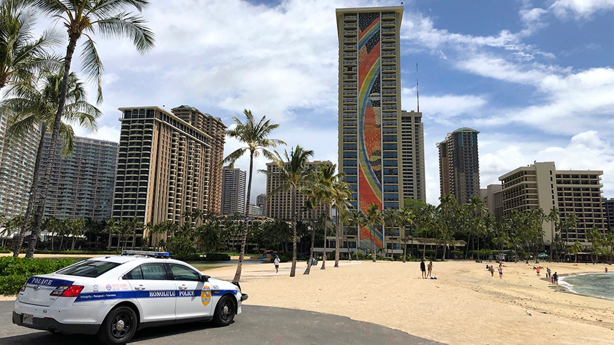 A police officer arrives to tell people to leave Waikiki Beach in Honolulu. Hawaii law enforcement authorities are cracking down on rogue tourists who are visiting beaches, jetskiing, shopping and generally flouting strict requirements that they quarantine for 14 days after arriving. (AP Photo/Caleb Jones, File)