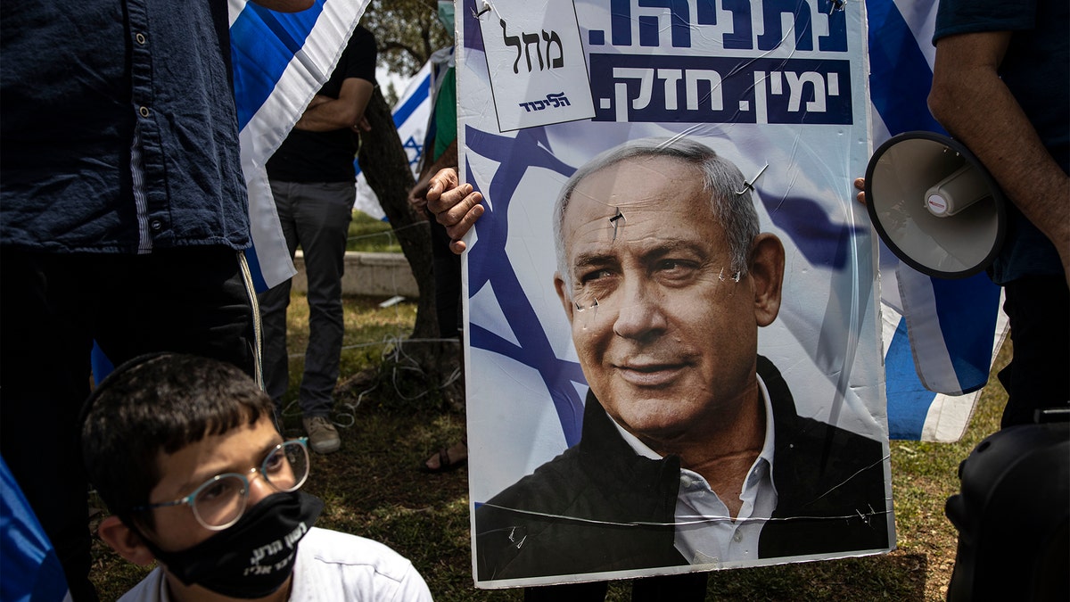An Israeli protester wears a mask amid concerns over the country's coronavirus outbreak looks on a poster of Prime Minister Benjamin Netanyahu during a protest by supporters of Netanyahu in front of Israel's Supreme Court in Jerusalem, Sunday, May 3, 2020. (AP Photo/Tsafrir Abayov)