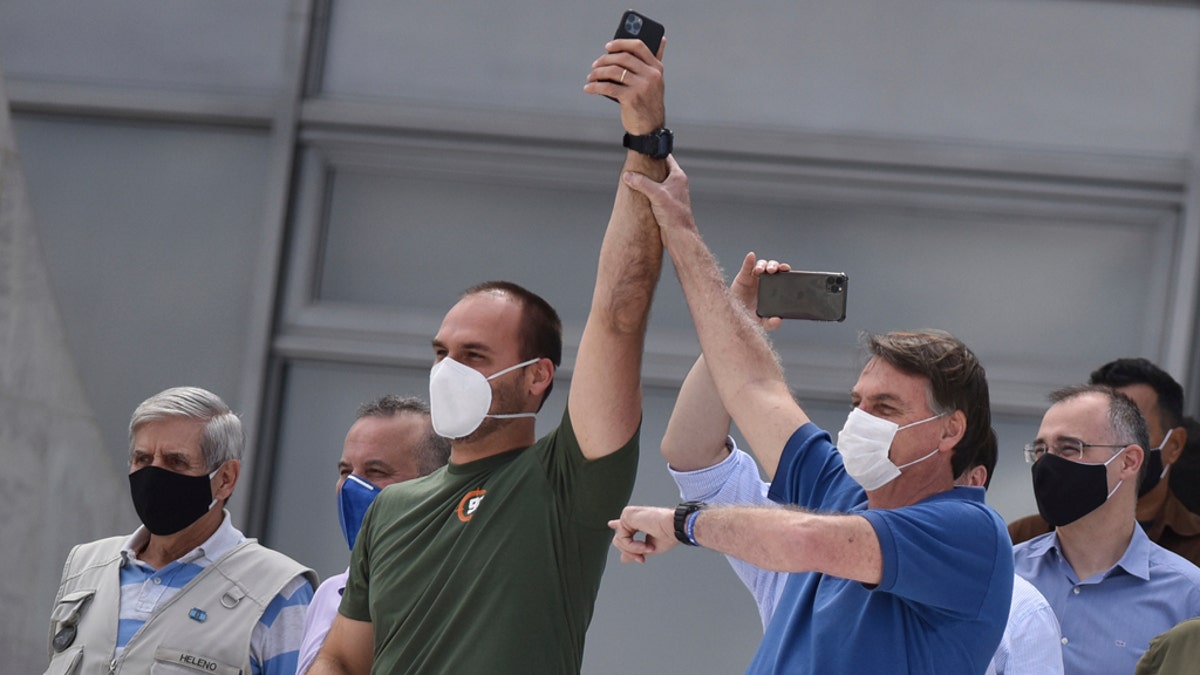 Brazil's President Jair Bolsonaro, right, wearing a mask against the spread of the new coronavirus, raises the arm of his son Eduardo Bolsonaro during a protest against the Supreme Court and Brazil's National Congress, and to back his open-the-economy drive amid the pandemic, in Brasilia, Brazil, Sunday, May 17, 2020. Bolsonaro greeted hundreds of supporters who gathered at the presidential residence to back his open-the-economy drive even as the COVID-19 pandemic sweeps across the country. (AP Photo/Andre Borges)