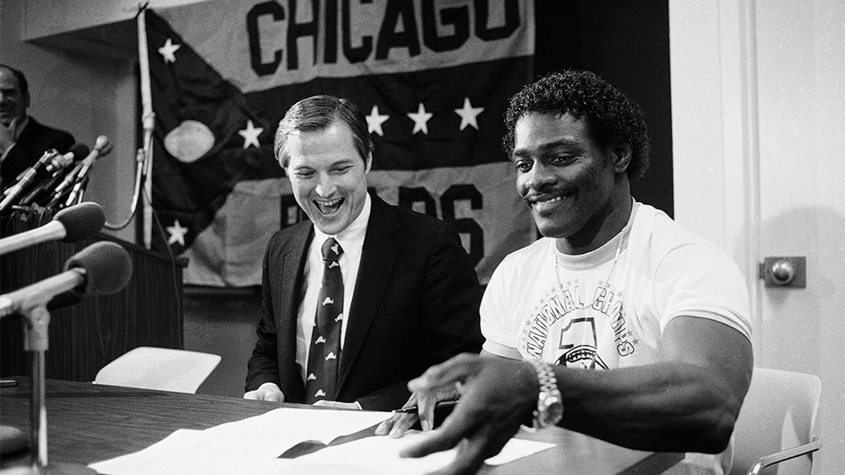 FILE - In this Tuesday, May 8, 1984, file photo, Walter Payton, right, a veteran Chicago Bears player and one of the National Football League's premiere running backs, signs three 1-year contracts as Mike McCaskey, president of the Chicago Bears, smiles during the news conference at the Bears' NFL football summer training camp in Lake Forest, Ill. (AP Photo/John Swart, File)