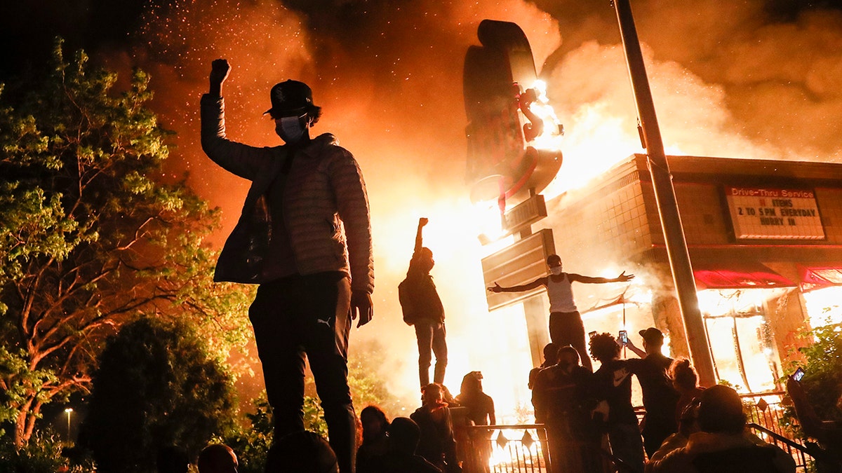 Protestors demonstrate outside of a burning fast food restaurant, Friday, May 29, 2020, in Minneapolis. Protests over the death of George Floyd, a black man who died in police custody Monday, broke out in Minneapolis for a third straight night. (AP Photo/John Minchillo)