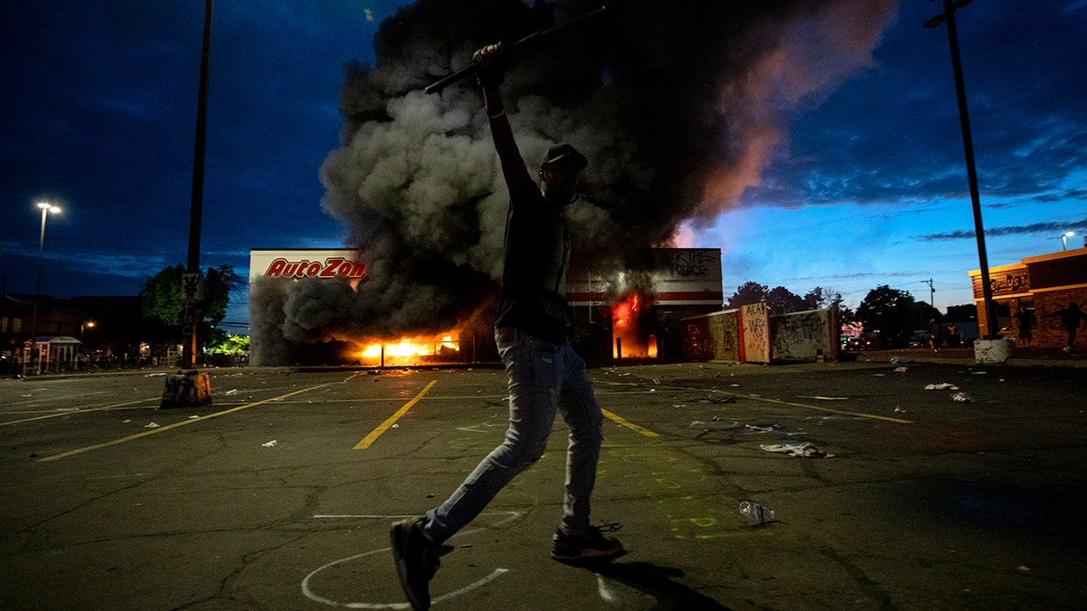 A man poses in the parking lot of an AutoZone store in flames, while protesters hold a rally against the death of George Floyd in Minneapolis on May 27. (Carlos Gonzalez/Star Tribune via AP)