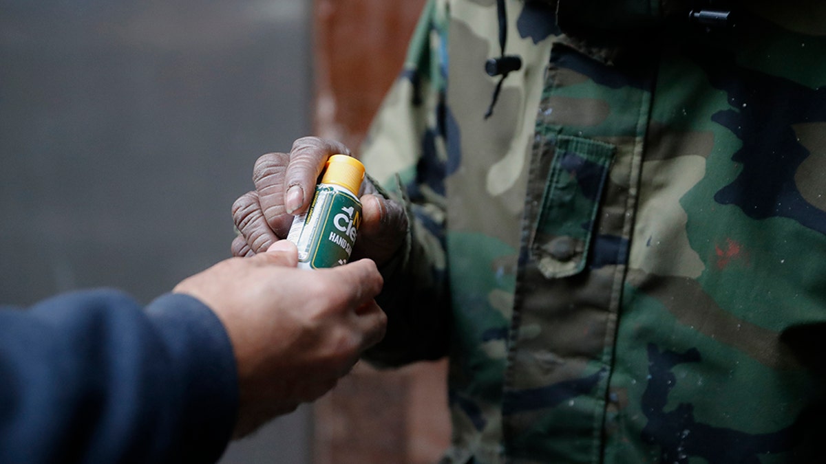 In this Friday, April 24, 2020, photo, Juan De La Cruz, left, hands a bottle of hand sanitizer to a visitor who collected a bag of donated food through the Coalition for the Homeless organization at St. Bartholomew's Episcopal Church in New York. (AP Photo/John Minchillo)