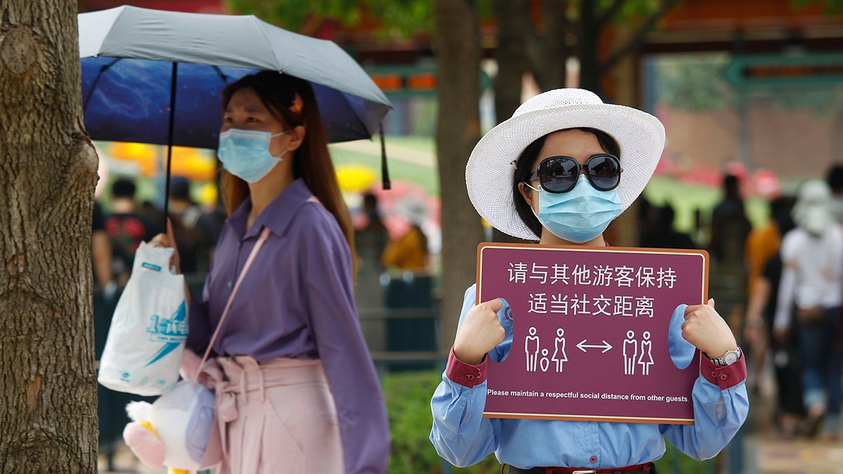 An employee holds a sign instructing guests to maintain safe social distancing on opening day.