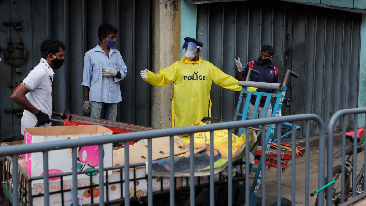 A Sri Lankan police officer in protective suit directs porters outside a market place in Colombo, Sri Lanka, on May 11.