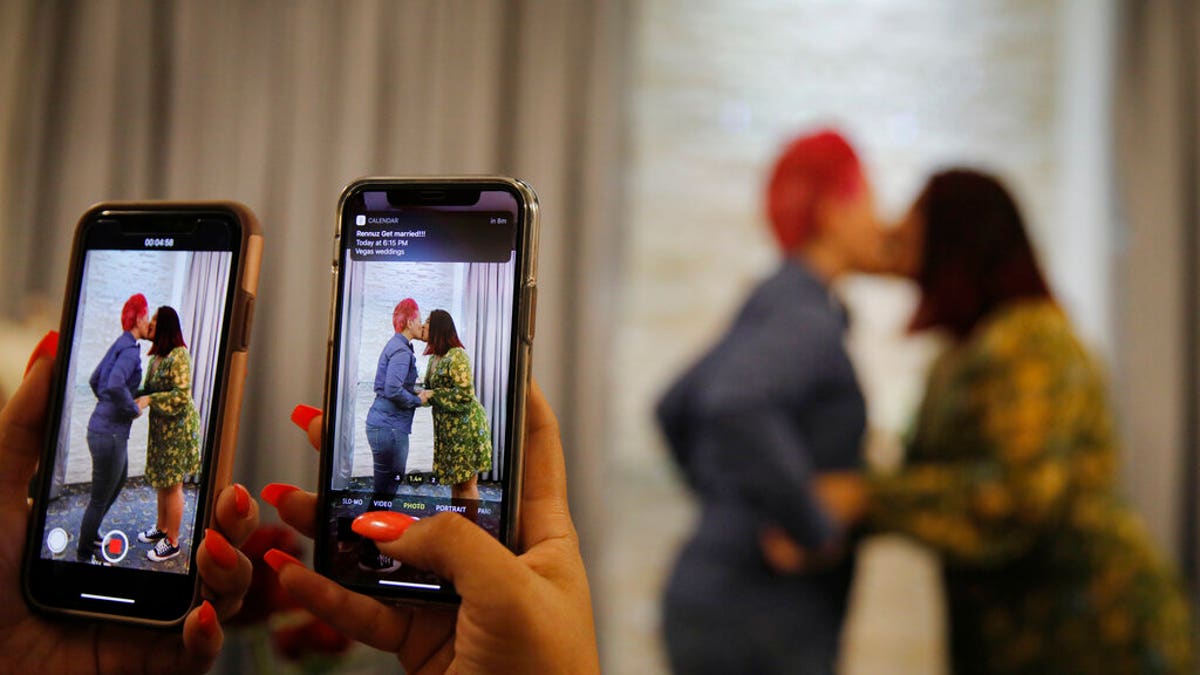 Cynthia Sanchez takes video and pictures as her sister Jennifer Escobar, right, and Luz Sigman celebrate their wedding ceremony at Vegas Weddings. (AP Photo/John Locher)