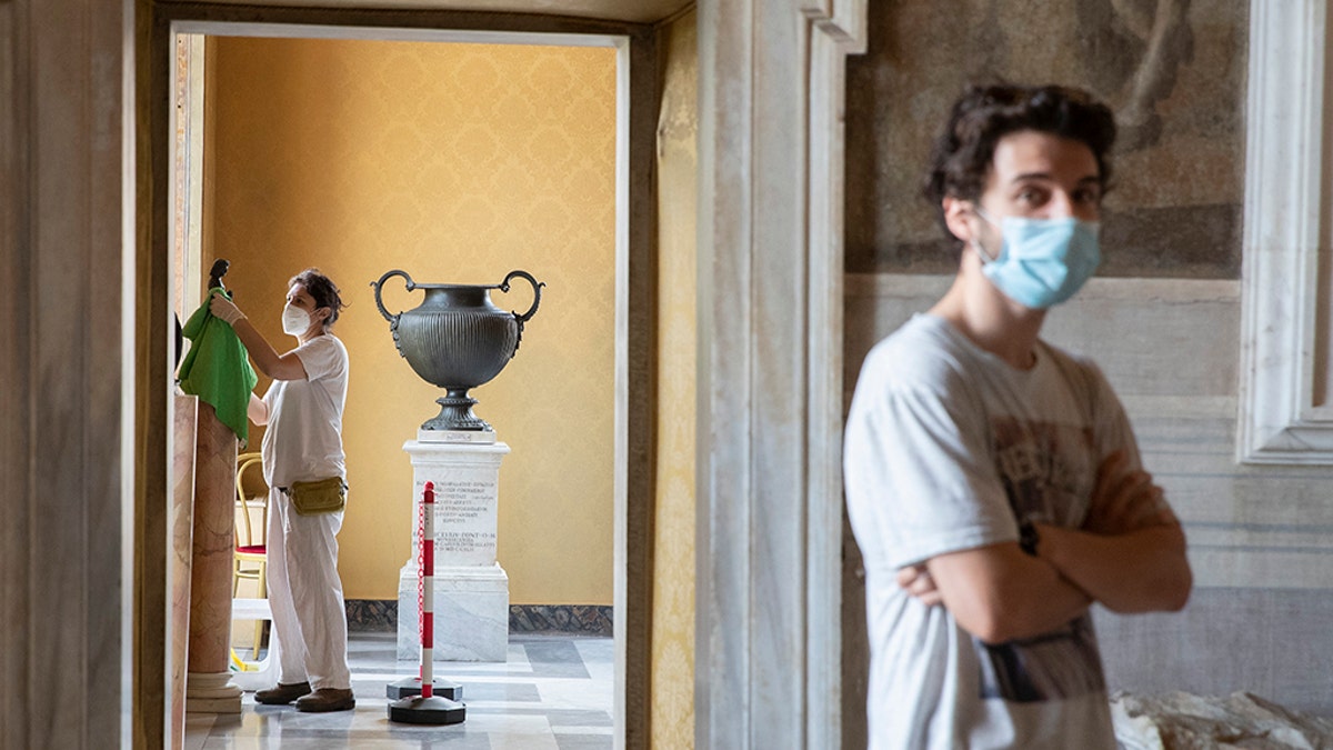 A museum employee cleans a statue, as a visitor wearing face mask to prevent the spread of COVID-19 walks in the Rome's Capitoline Museums, Tuesday, May 19, 2020. (AP Photo/Alessandra Tarantino)