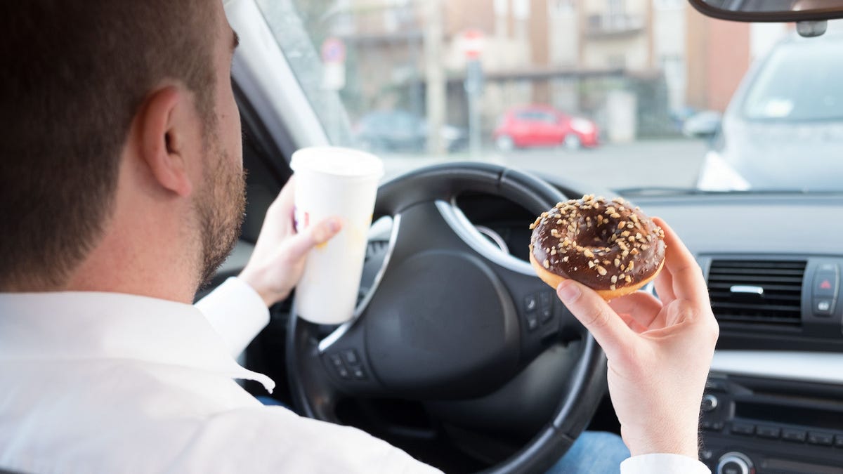 Man having breakfast and driving seated in car