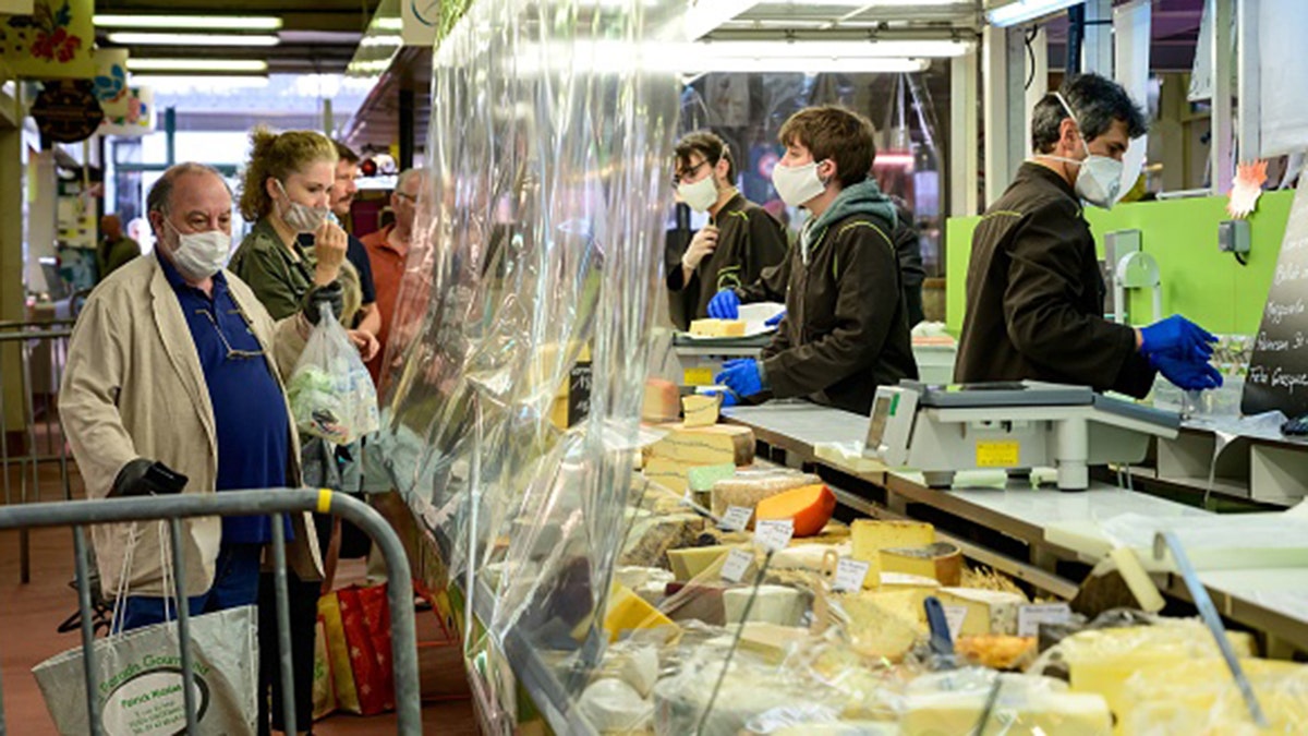 Customers, wearing protective facemasks, queue at the cheese counter in order to be served behind a transparent plastic curtain at a covered market in Le Perreux-sur-Marne on April 19. (BERTRAND GUAY/AFP via Getty Images)